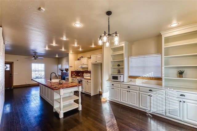 kitchen featuring wooden counters, decorative light fixtures, stainless steel range with electric stovetop, a kitchen island with sink, and white cabinets