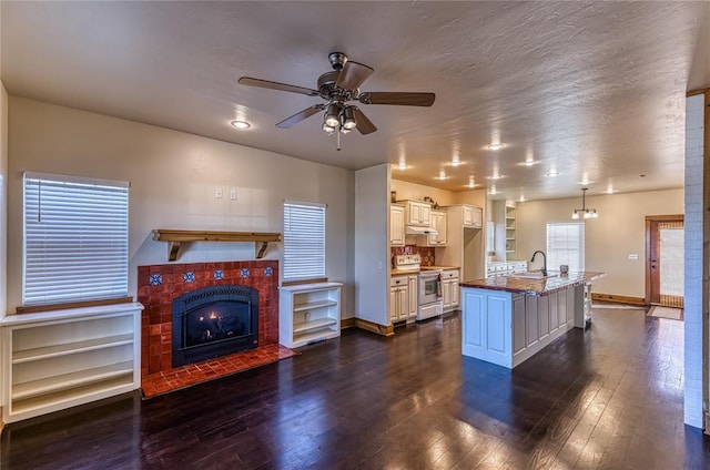 kitchen with baseboards, dark wood finished floors, a tiled fireplace, a sink, and range with electric stovetop