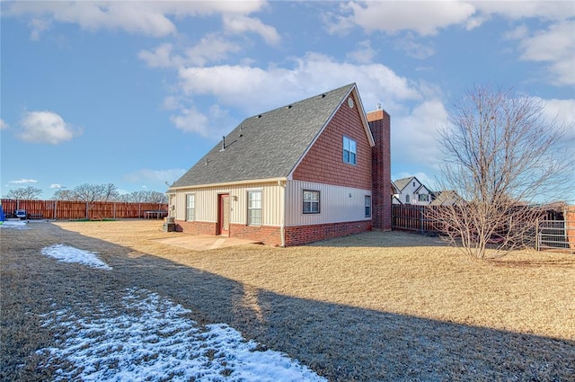 rear view of property featuring brick siding, a yard, a chimney, roof with shingles, and a fenced backyard