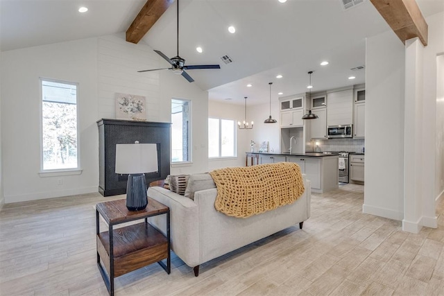 living room with ceiling fan with notable chandelier, lofted ceiling with beams, light hardwood / wood-style flooring, and sink