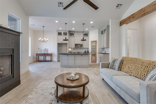 living room with vaulted ceiling with beams, light hardwood / wood-style floors, and ceiling fan with notable chandelier