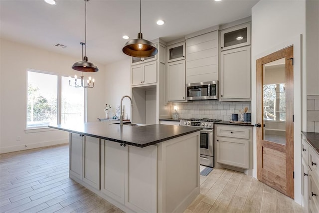 kitchen featuring sink, backsplash, decorative light fixtures, a center island with sink, and appliances with stainless steel finishes