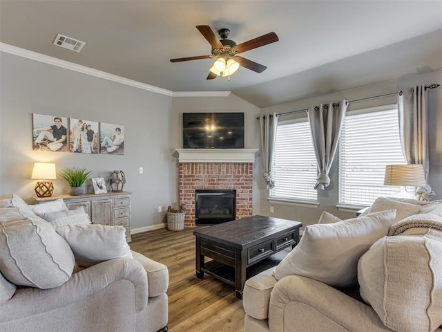 living room featuring ceiling fan, a brick fireplace, lofted ceiling, crown molding, and light hardwood / wood-style flooring