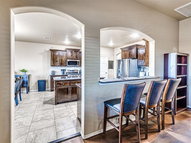 kitchen with kitchen peninsula, dark brown cabinets, backsplash, and stainless steel appliances