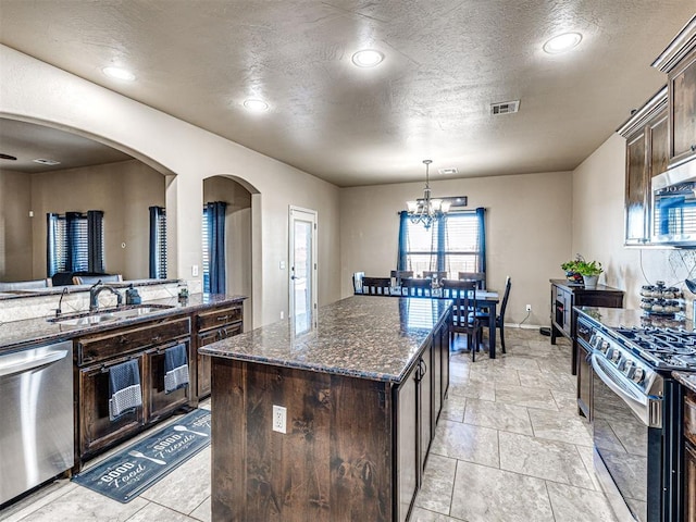 kitchen featuring dark stone counters, dark brown cabinets, stainless steel appliances, a notable chandelier, and a kitchen island