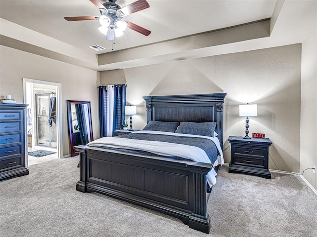 carpeted bedroom with a raised ceiling, connected bathroom, and ceiling fan