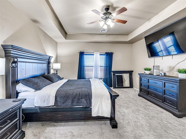 carpeted bedroom with a raised ceiling and ceiling fan