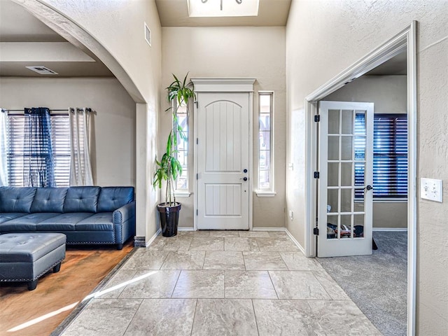 carpeted foyer entrance with visible vents, arched walkways, and a healthy amount of sunlight