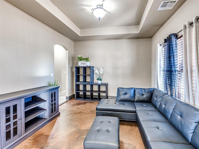 living area with a raised ceiling, visible vents, arched walkways, and baseboards