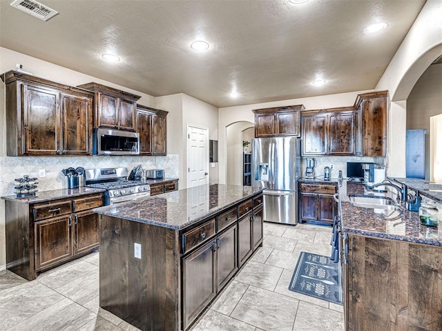 kitchen featuring dark stone countertops, arched walkways, appliances with stainless steel finishes, and a sink