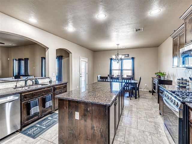 kitchen featuring visible vents, dark brown cabinets, dark stone counters, arched walkways, and stainless steel appliances