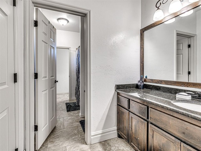 full bathroom featuring stone finish floor, vanity, baseboards, and a textured wall
