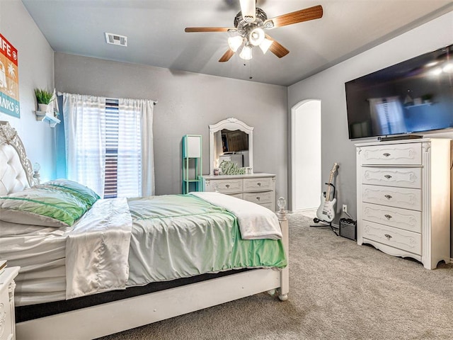 bedroom with light carpet, visible vents, arched walkways, and a ceiling fan