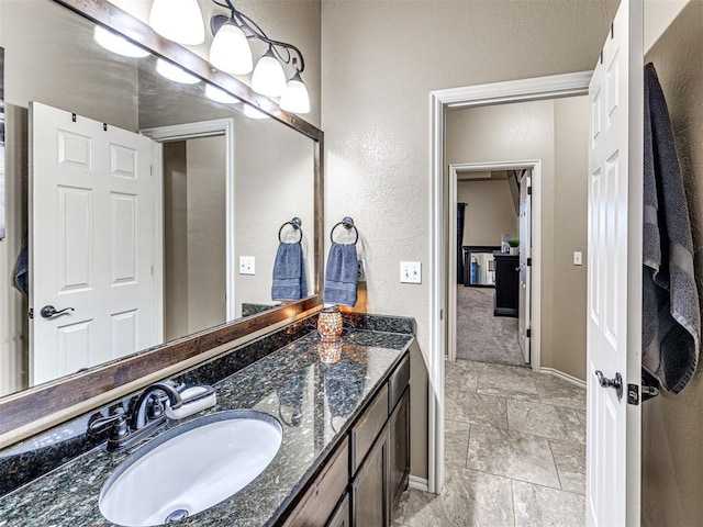 bathroom featuring stone finish floor, vanity, baseboards, and a textured wall