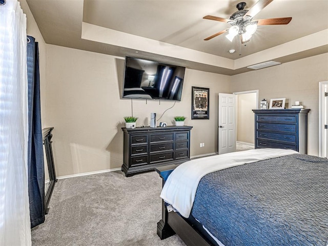 carpeted bedroom featuring a ceiling fan, a tray ceiling, visible vents, and baseboards