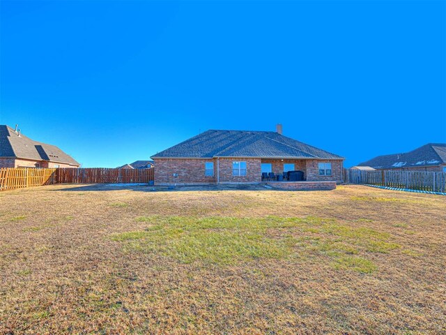 back of house featuring a yard, brick siding, and a fenced backyard