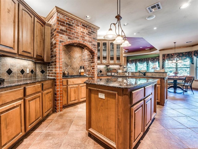 kitchen with a center island, backsplash, crown molding, dark stone countertops, and decorative light fixtures