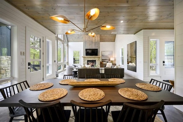 dining room with wooden ceiling, wooden walls, a wealth of natural light, and a stone fireplace