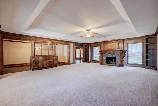 unfurnished living room with a raised ceiling, ceiling fan, a fireplace, and carpet floors