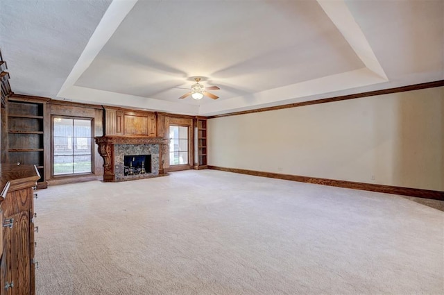 unfurnished living room with ceiling fan, a wealth of natural light, light carpet, and a raised ceiling