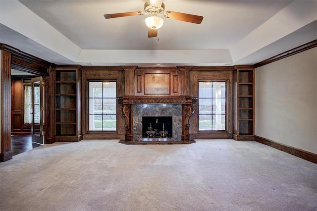 unfurnished living room with carpet, ceiling fan, a fireplace, a raised ceiling, and built in shelves