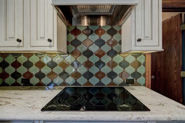 kitchen featuring light stone countertops, decorative backsplash, wall chimney exhaust hood, and black electric stovetop