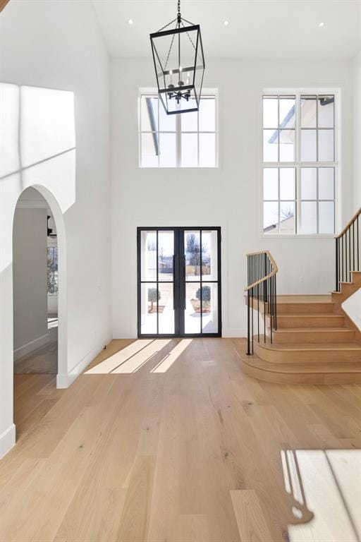 unfurnished living room with a towering ceiling, a chandelier, french doors, and light wood-type flooring