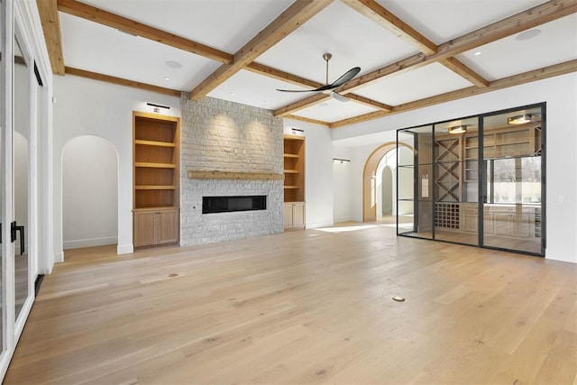 unfurnished living room with light hardwood / wood-style flooring, ceiling fan, built in features, a stone fireplace, and coffered ceiling