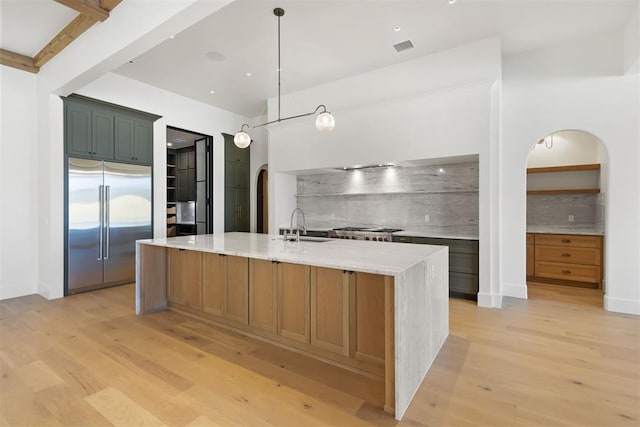 kitchen featuring appliances with stainless steel finishes, tasteful backsplash, hanging light fixtures, a kitchen island with sink, and light stone counters