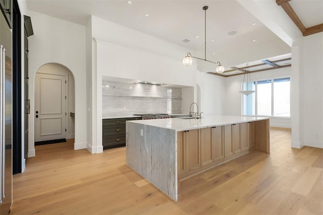 kitchen with an island with sink, sink, hanging light fixtures, light stone counters, and beam ceiling