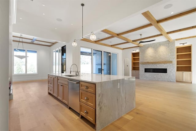 kitchen with light stone countertops, a kitchen island with sink, sink, built in shelves, and decorative light fixtures