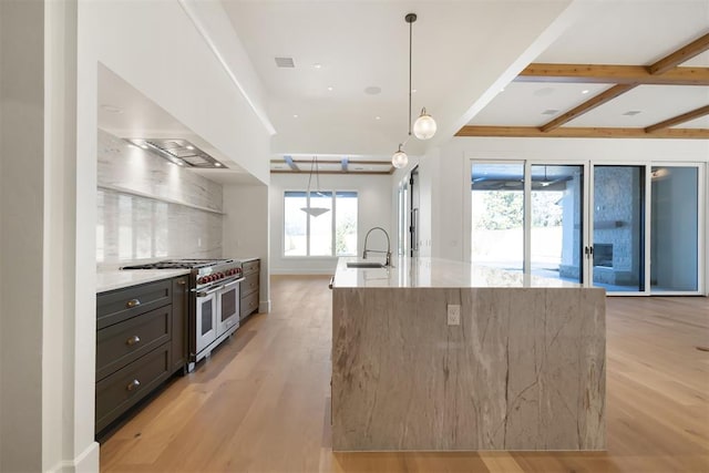 kitchen featuring decorative light fixtures, light hardwood / wood-style flooring, an island with sink, light stone counters, and range with two ovens