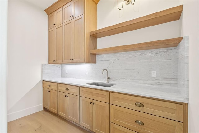 kitchen with light stone countertops, tasteful backsplash, light brown cabinetry, sink, and light hardwood / wood-style flooring