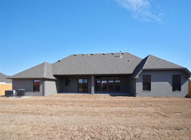 rear view of house with cooling unit, brick siding, fence, and roof with shingles