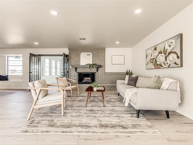 living room featuring a brick fireplace and light wood-type flooring