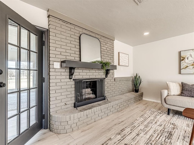 living room with light hardwood / wood-style floors, a brick fireplace, and a textured ceiling