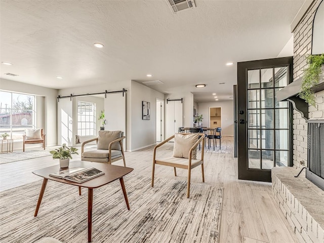 living room with a large fireplace, a barn door, and light hardwood / wood-style flooring