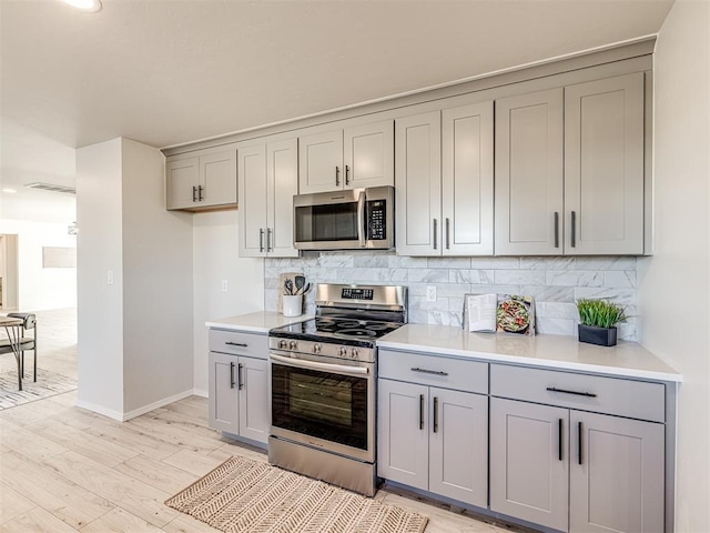 kitchen with stainless steel appliances, backsplash, gray cabinetry, and light hardwood / wood-style flooring