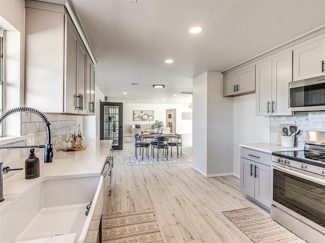 kitchen featuring gray cabinets, stainless steel appliances, light wood-type flooring, decorative backsplash, and sink