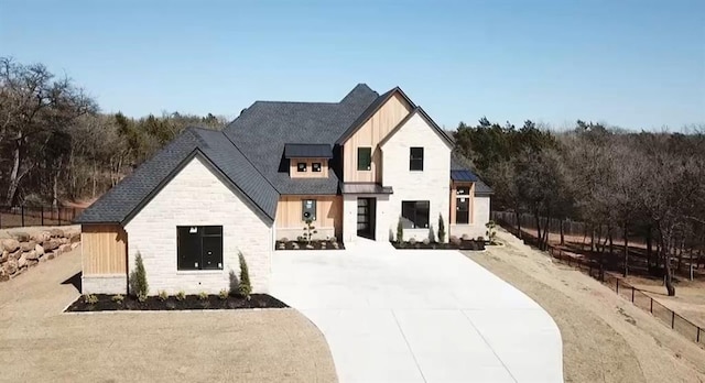 modern farmhouse featuring board and batten siding, fence, metal roof, stone siding, and a standing seam roof