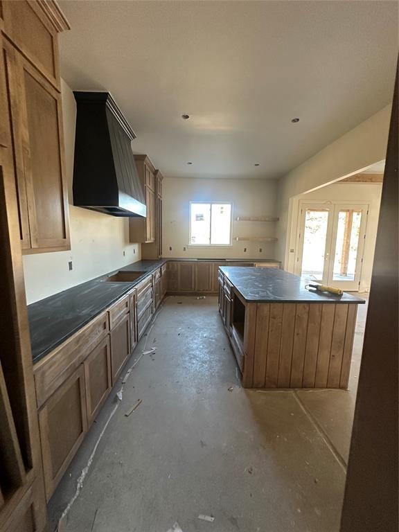 kitchen with dark countertops, a kitchen island, concrete flooring, custom range hood, and french doors