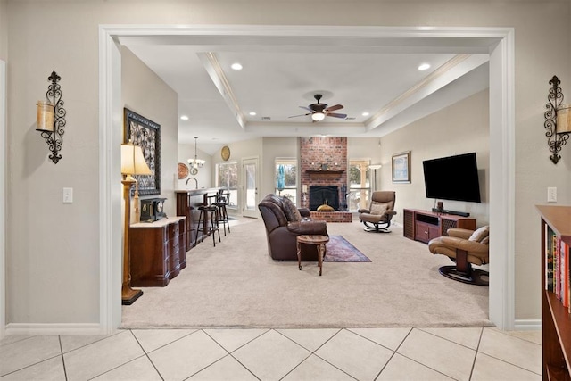 carpeted living room featuring a fireplace, a raised ceiling, ceiling fan, and crown molding