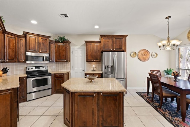 kitchen with light stone countertops, a center island, stainless steel appliances, an inviting chandelier, and light tile patterned floors