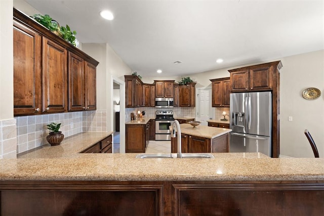 kitchen featuring backsplash, sink, appliances with stainless steel finishes, dark brown cabinets, and kitchen peninsula