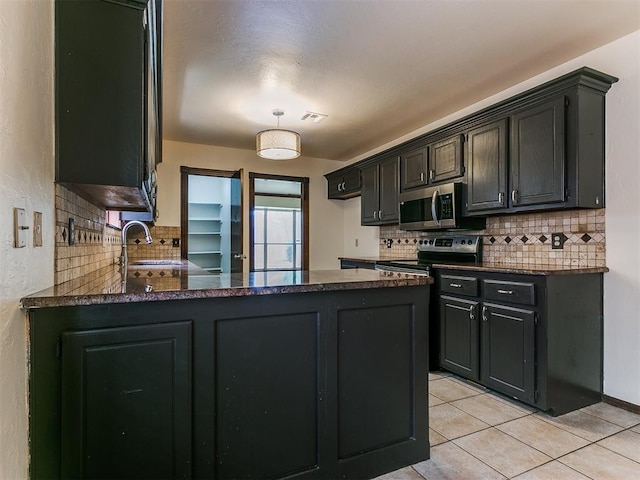 kitchen with sink, backsplash, kitchen peninsula, light tile patterned floors, and appliances with stainless steel finishes