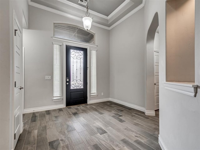 foyer with wood-type flooring, a raised ceiling, and crown molding