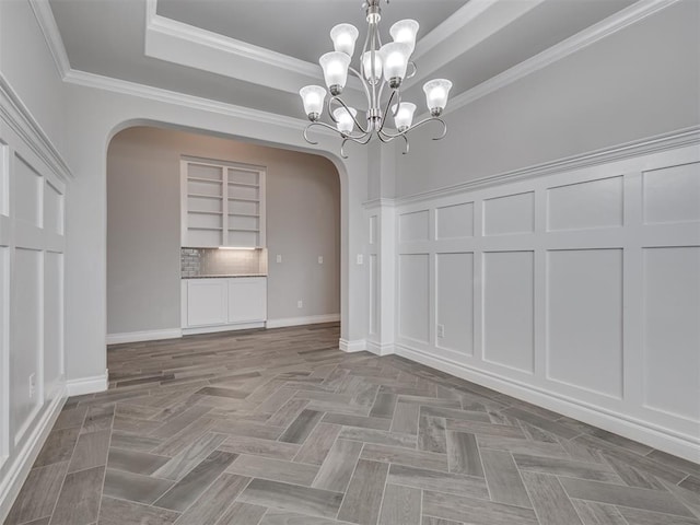 unfurnished dining area featuring a tray ceiling, parquet floors, ornamental molding, and an inviting chandelier