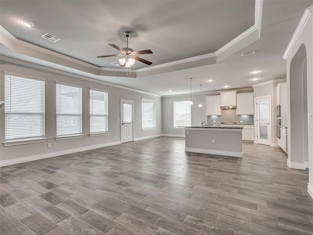 unfurnished living room featuring a raised ceiling, ceiling fan, light hardwood / wood-style flooring, and ornamental molding