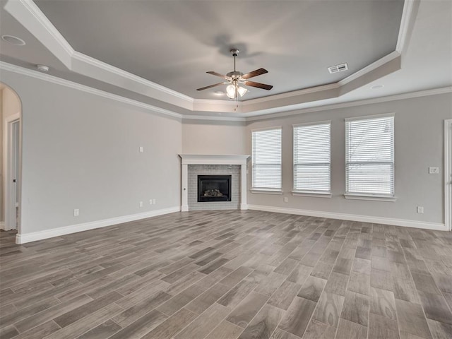 unfurnished living room with a fireplace, a healthy amount of sunlight, a raised ceiling, and crown molding