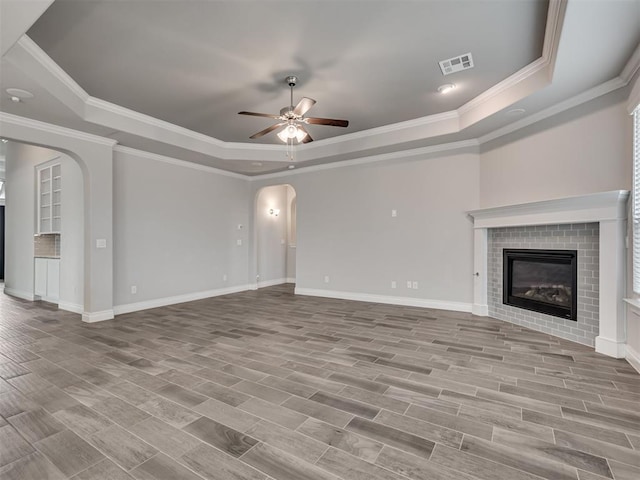 unfurnished living room with a tile fireplace, a tray ceiling, ceiling fan, and ornamental molding